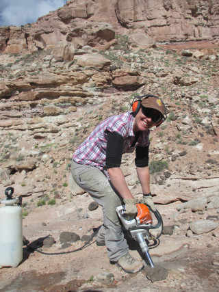 Susannah operates a jackhammer while digging in the desert. 