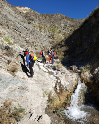 A team of researchers stands in a deep valley alongside a creek.