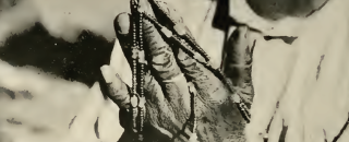 A histoire photo of a pair of hands holding a strand of shell beads.