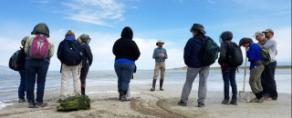 A group of teachers listen to an instructor on the sandy shoreline of the Great Salt Lake