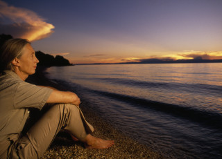 Dr. Jane Goodall sits on a beach in Gombe National Park at sunset. 