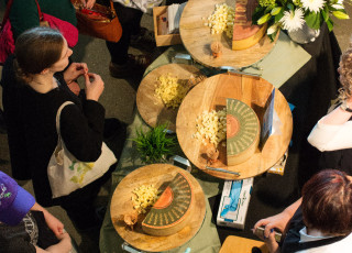 An overhead shot of people looking at cheese on boards